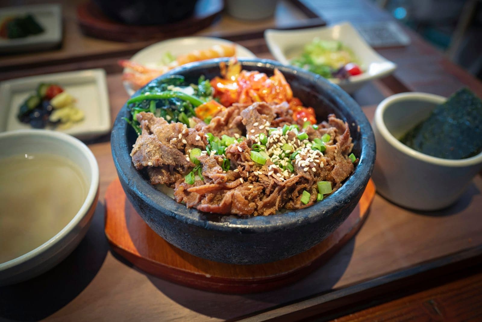 Marinated sliced beef with scallions and sesame seeds over rice, with Korean side dishes