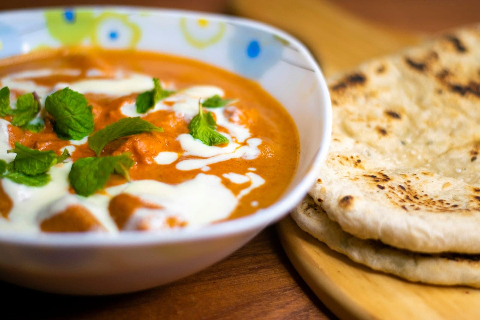 A bowl of creamy butter chicken with a swirl of cream and mint, served with naan