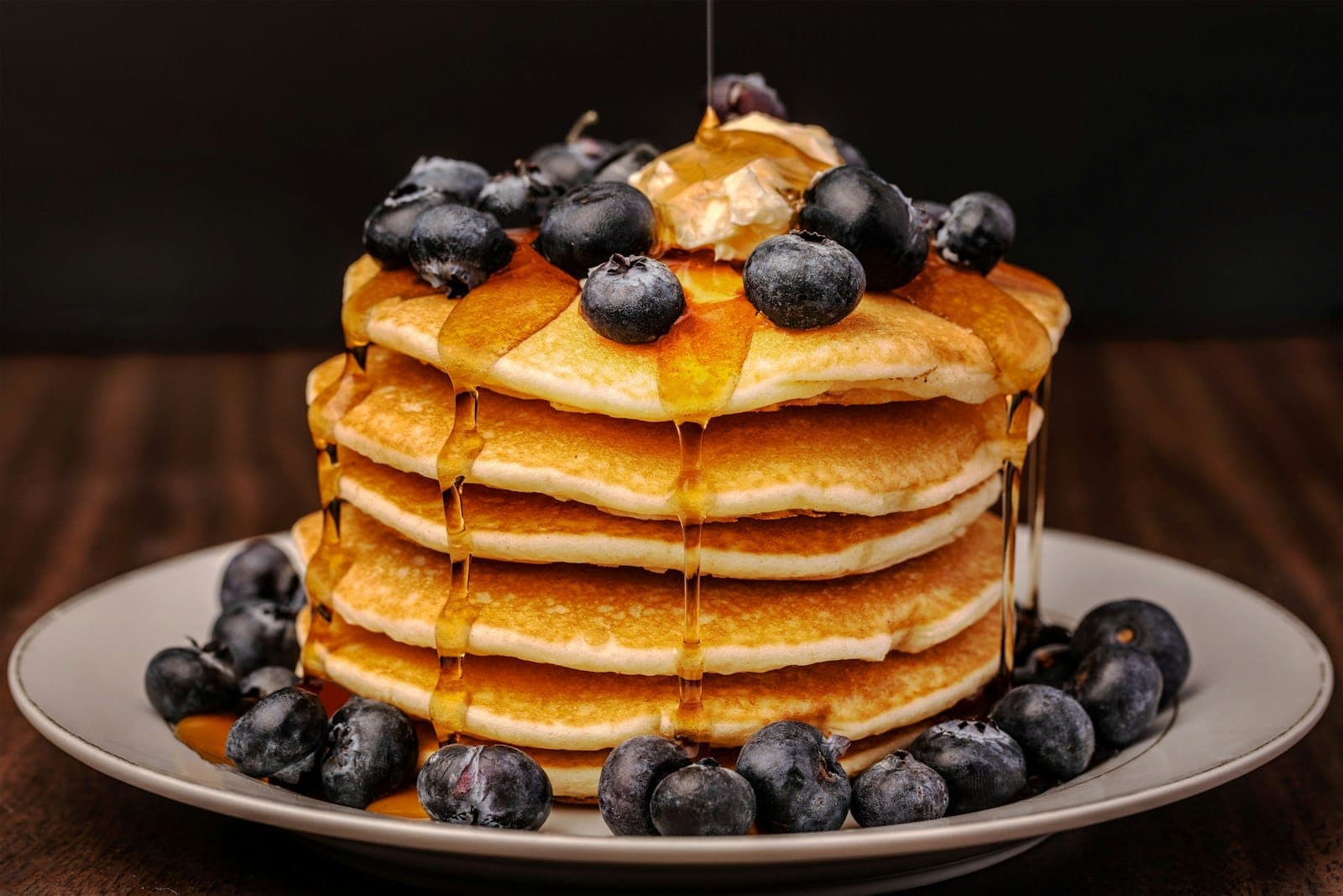 A tall stack of pancakes with blueberries and syrup