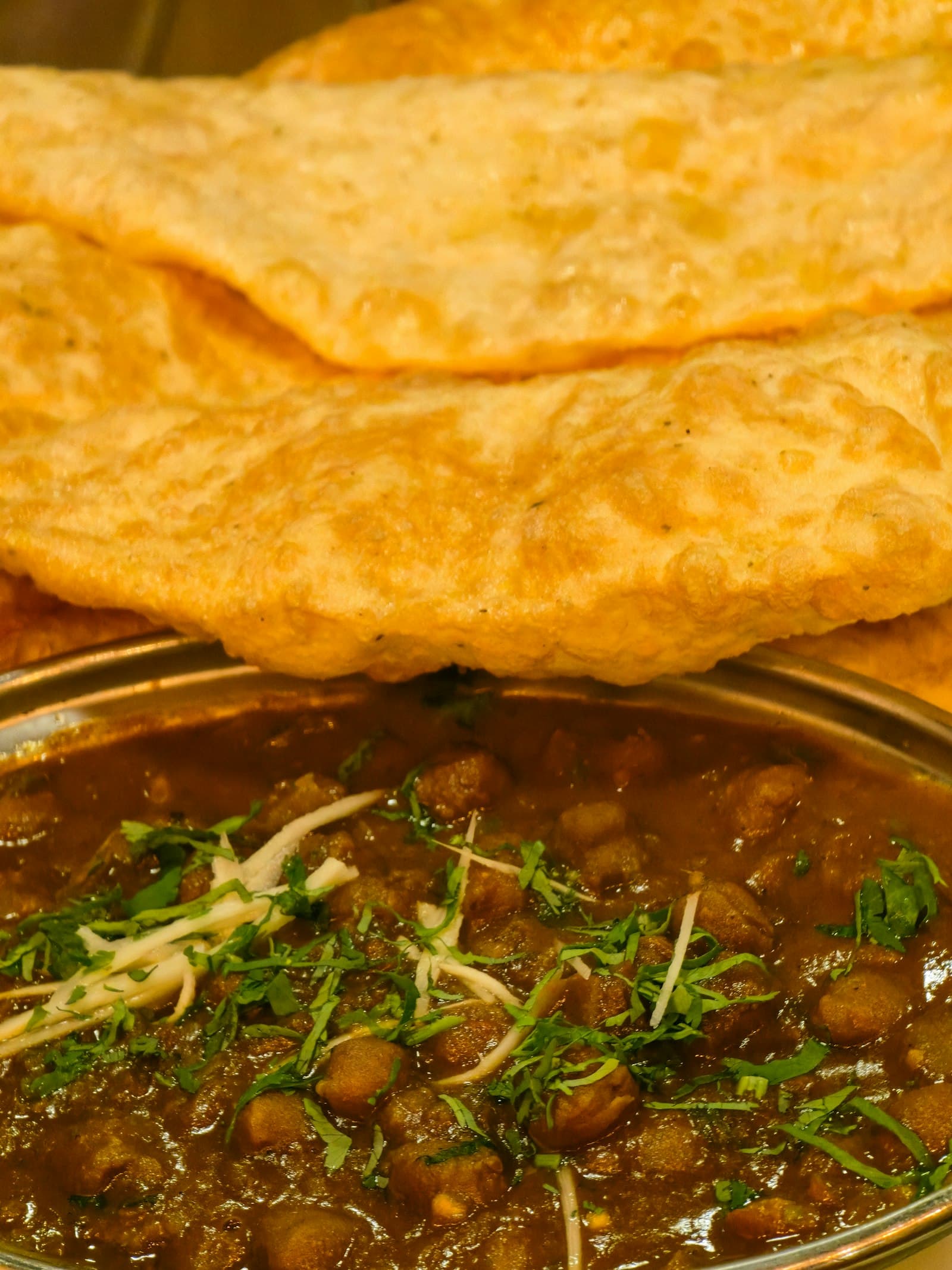 A bowl of chana masala garnished with cilantro and ginger, served with fried bread
