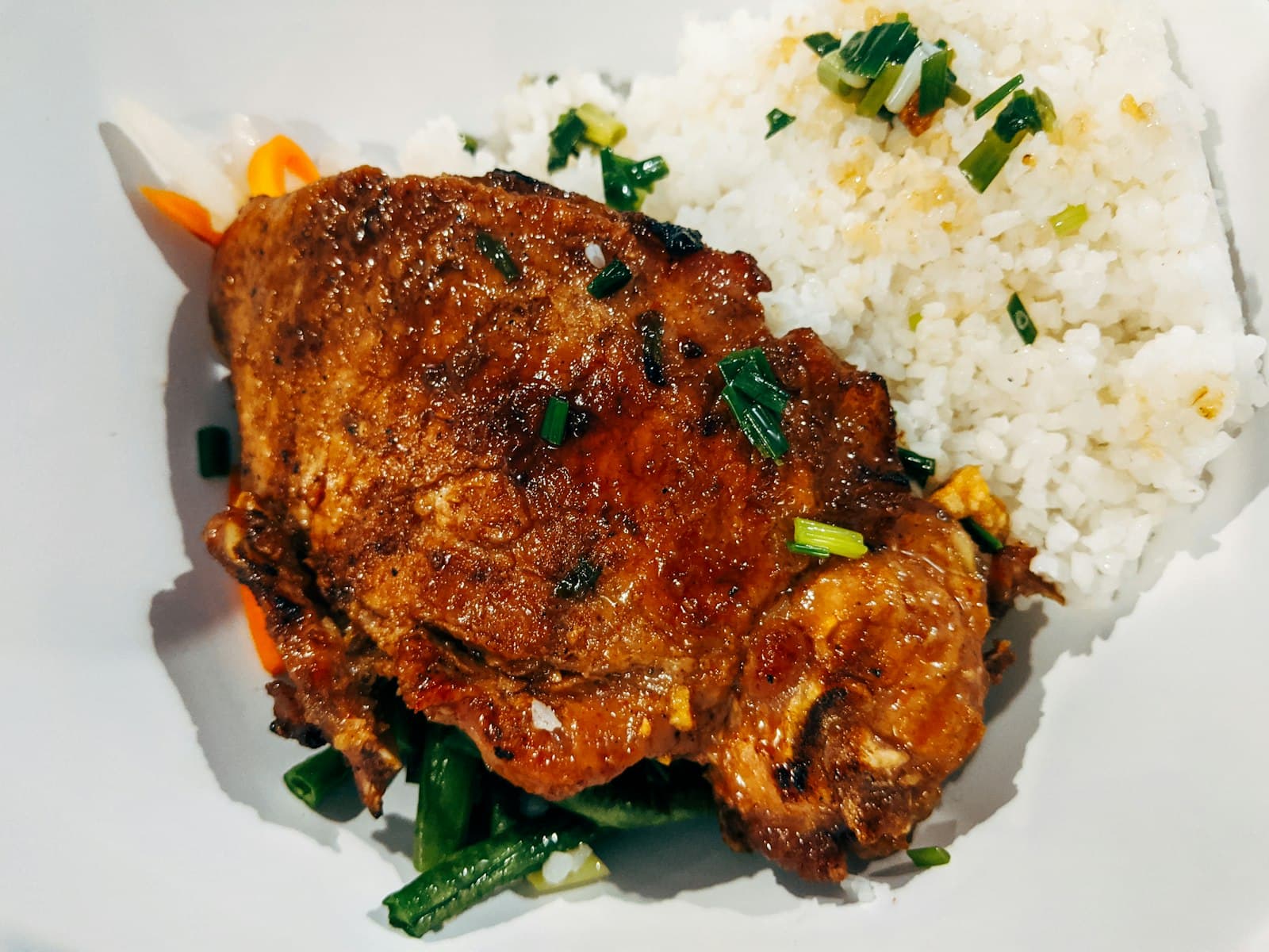 A braised chicken thigh in a dark, glossy sauce with white rice