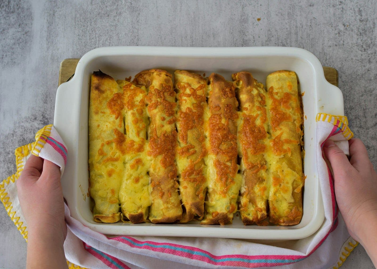 A baking dish of rolled enchiladas under golden melted cheese