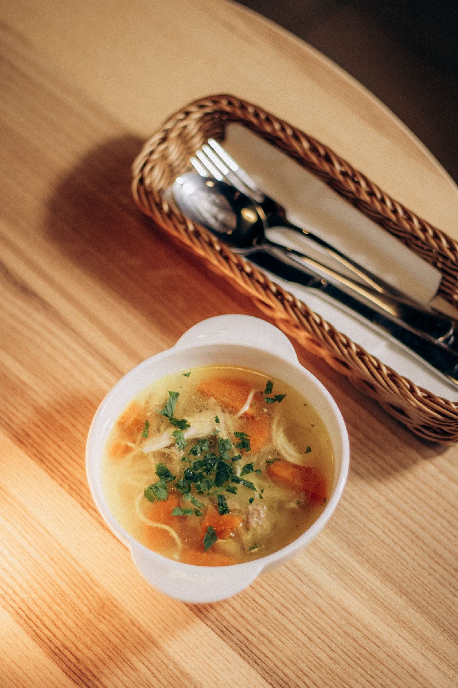 A bowl of chicken noodle soup with carrots and fresh herbs