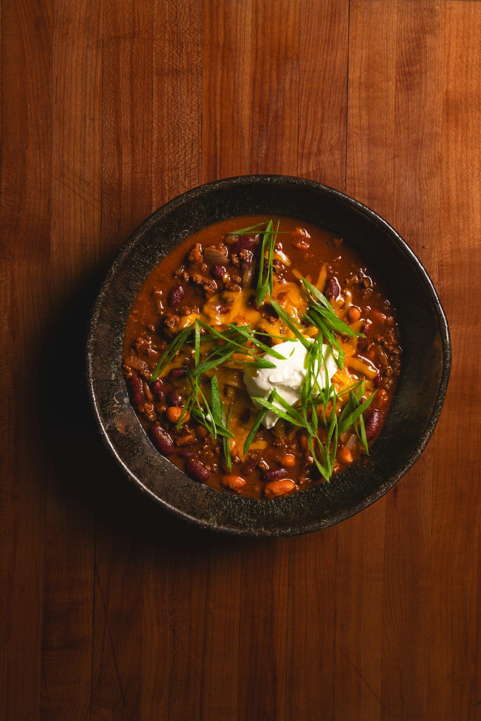 A bowl of beef and bean chili topped with cheddar, sour cream and scallions
