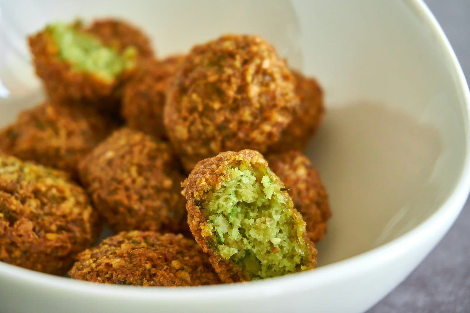 Crisp falafel in a bowl, one broken open to show the green herb filling