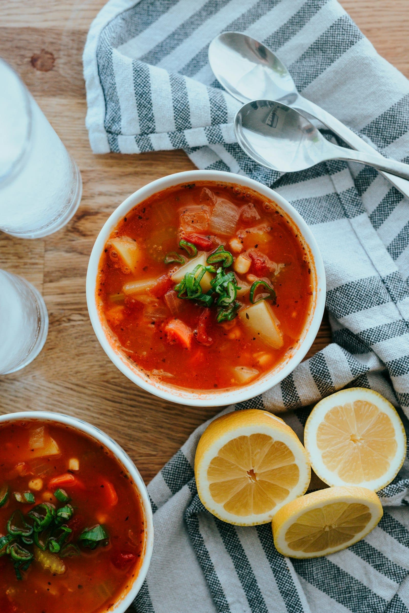 Bowls of tomato vegetable soup with beans, served with lemon halves