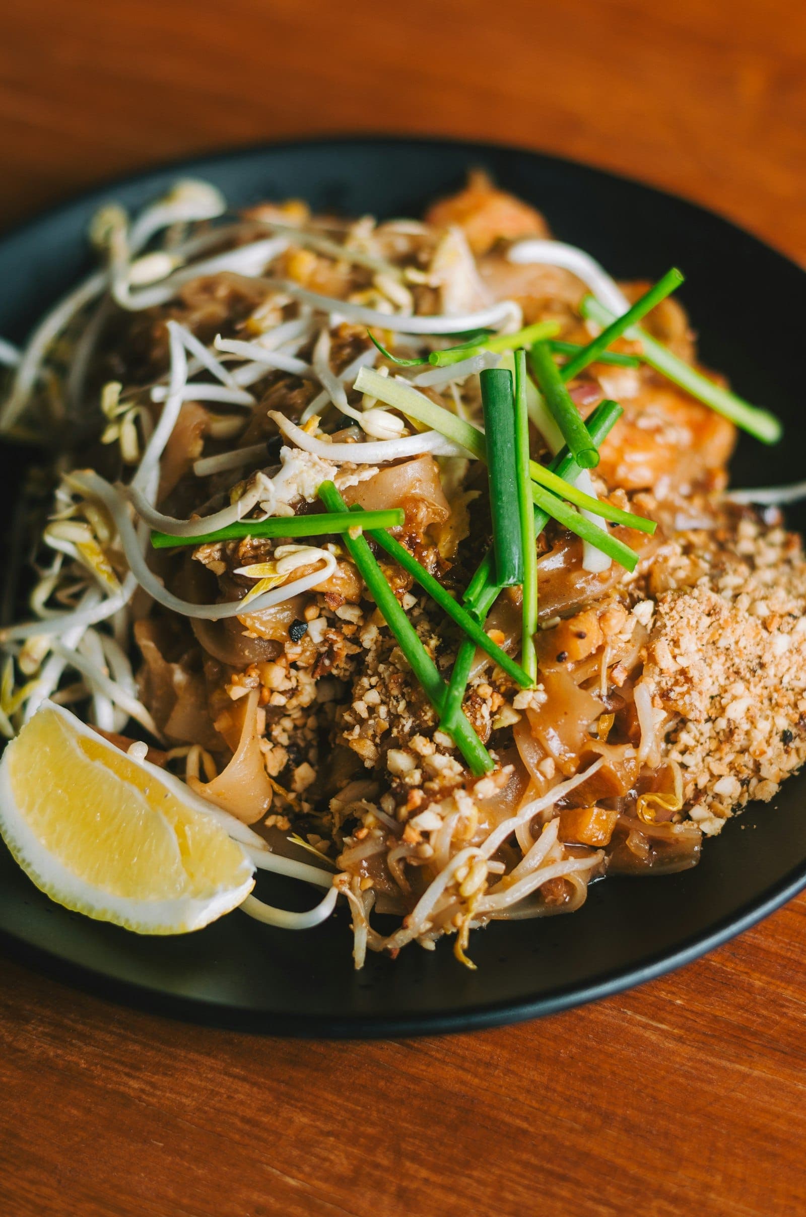 Pad thai topped with crushed peanuts, bean sprouts and chives, with a lemon wedge